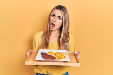 Güzel İspanyol kadın elinde rulo köfte ve kızarmış yumurta ile şok suratlı, şüpheci ve alaycı görünüyor, ağzı açık şaşırmış 