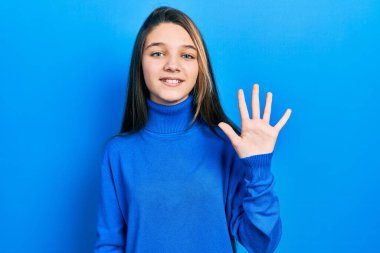 Balıkçı yaka kazak giyen genç esmer kız beş numarayı gösterip işaret ederken kendinden emin ve mutlu bir şekilde gülümsüyor.. 