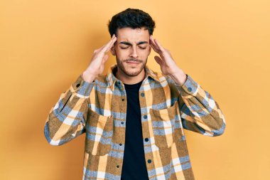 Latin asıllı genç bir adam elleri kafasında günlük kıyafetler giyiyor, stres yüzünden baş ağrısı çekiyor. migren ağrısı. 