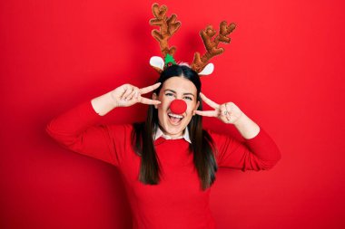 Geyik şapkası takan genç İspanyol kadın ve kırmızı burun barış sembolü yapıyor. Yüzünde parmaklar, gülümseyerek zaferi gösteriyor. 