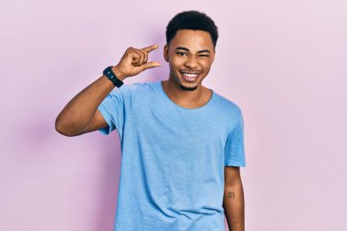 Genç, Afro-Amerikan bir adam, günlük mavi tişört giyiyor gülümsüyor ve el hareketleriyle el hareketi yapıyor, parmaklarıyla işaret yapıyor ve kameraya bakıyor. ölçüm kavramı. 