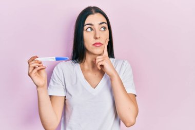 Elinde hamilelik testi olan mavi gözlü güzel bir kadın ciddi bir yüzle soru sorarken çenesi üzerine kafa karıştırıcı bir fikir hakkında düşünceli. 