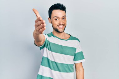Gündelik kıyafetler giyen genç İspanyol adam dostça bir selamlama ve hoş geldin hediyesi olarak el sıkışmayı sunuyor. başarılı iş. 