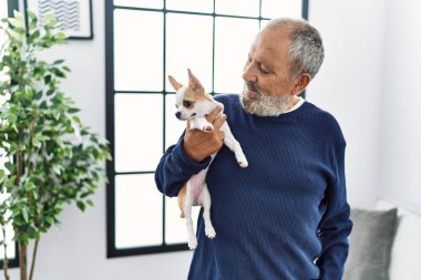 Yaşlı, gri saçlı, gülümseyen ve elinde Chihuahua tutan adam.