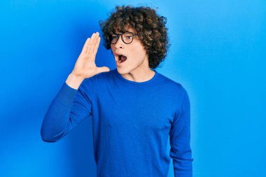 Sıradan kıyafetler ve gözlük takan yakışıklı genç adam el ve ağızla bağırıyor ve yüksek sesle bağırıyor. iletişim konsepti. 