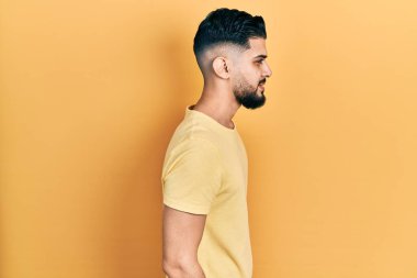 Sakallı, sıradan sarı tişörtlü, rahat profil pozu veren, kendine güveni olan yakışıklı bir adam.. 