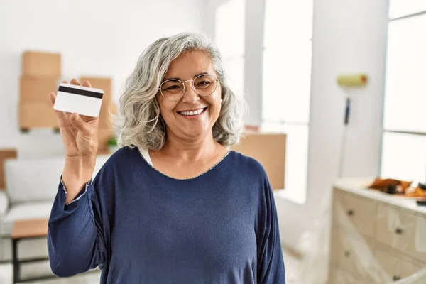 Middle age grey-haired woman smiling happy holding credit card at new home.