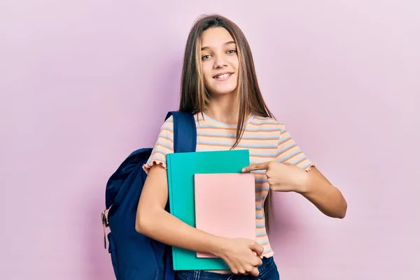 年轻的黑发女孩拿着学生的背包和书本 开心地微笑着 手指手画脚 — 图库照片