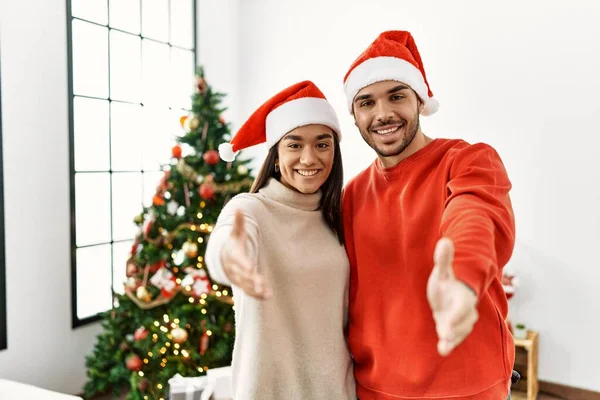 他的年轻夫妇站在圣诞树旁 友好地微笑着 握手致意和欢迎 成功的商业 — 图库照片