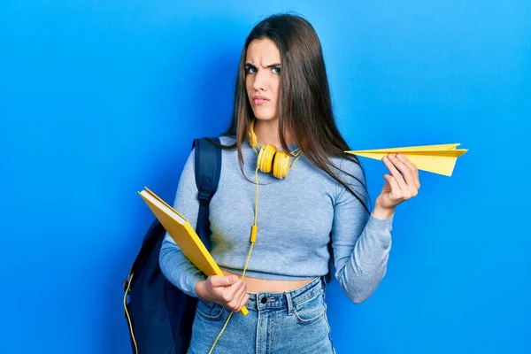 Elinde kitap ve kağıttan uçak tutan genç esmer bir öğrenci. Hiçbir şeyden habersiz ve kafası karışmış bir ifade. şüphe kavramı. 