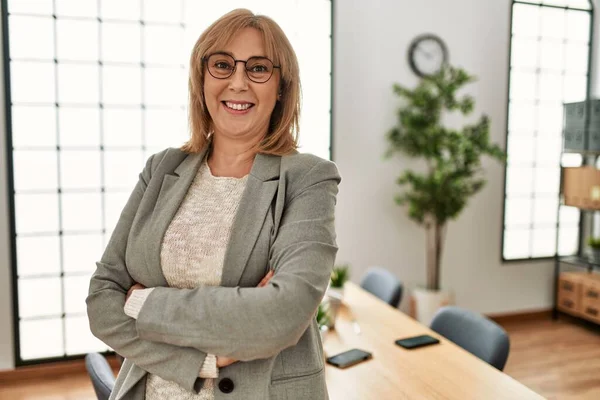 Middle age businesswoman smiling happy standing with arms crossed gesture at the office.