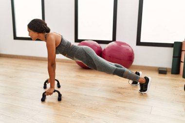 Genç Latin kadın gülümsüyor spor merkezinde kendine güvenen şınav çekiyor.