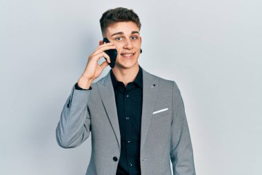 Kulakları genişlemiş beyaz bir çocuk akıllı telefondan konuşuyor. Olumlu ve mutlu görünüyor. Kendine güvenen bir gülümsemeyle dişlerini gösteriyor. 