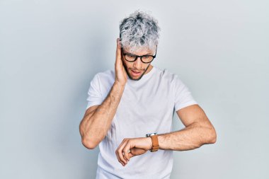 Modern boyalı saçlı, beyaz tişörtlü, gözlüklü, endişeli, geç kalmaktan korkan genç İspanyol bir adam. 