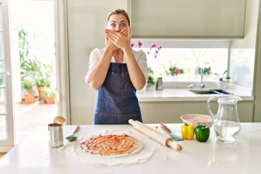 Önlük takan güzel sarışın kadın pizza pişirirken ağzını yanlışlıkla ellerle kapatırken şok oldu. gizli kavram. 