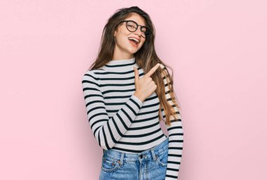 Gündelik kıyafetler ve gözlük takan genç ve güzel bir kız. Yüzünde mutlu ve doğal bir ifadeyle elleri ve parmaklarıyla gülümseyen bir gülümseme. 