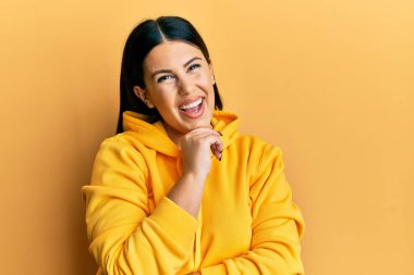 Güzel esmer kadın, sıradan bir kazak giyiyor, gülümsüyor ve kameraya kollarını kavuşturup çenesine bakıyor. Olumlu düşünmek. 