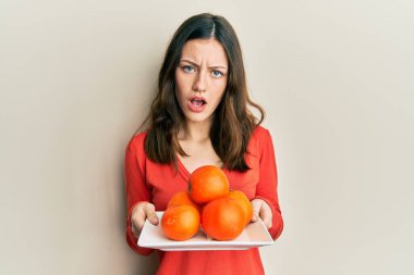 Genç esmer kadın elinde taze portakallı bir tabakla kuşkucu ve alaycı görünüyor, ağzı açık kalınca şaşırıyor. 