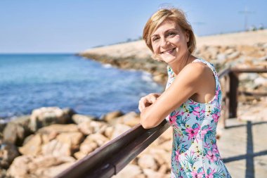 Orta yaşlı, güzel bir kadın. Deniz kenarında kendine güvenen.