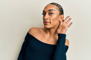 Makyaj yapan, uzun saçlı, kadın kıyafetleri giyen, ağzı kulaklarında gülümseyen dedikoduları ve dedikoduları dinleyen İspanyol bir adam. Sağırlık kavramı. 