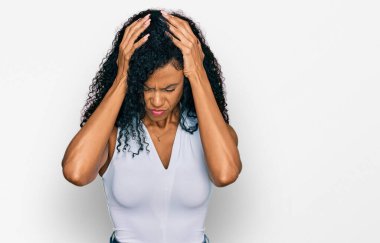 Orta yaşlı Afro-Amerikalı kadın kolsuz tişörtlü, gündelik giyiniyor. Ağrı ve migren yüzünden çaresiz ve stresli. Eller başının üstünde.. 