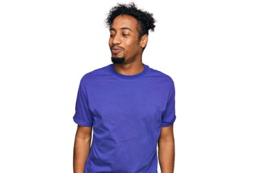 Sakallı, sıradan, mor tişörtlü genç bir Afro-Amerikalı. Gülümsüyor, yan tarafa bakıyor ve düşünüyor.. 