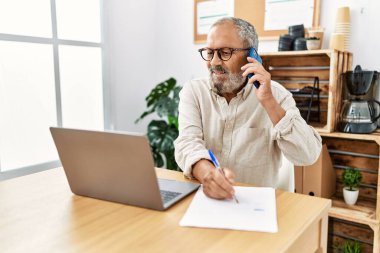 Ofiste çalışan yaşlı gri saçlı adam akıllı telefondan konuşuyor.