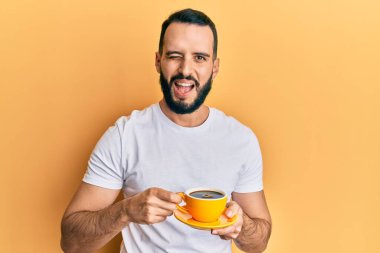 Sakallı, kahve içen, kameraya seksi bir ifadeyle bakan, neşeli ve mutlu yüzlü genç bir adam.. 