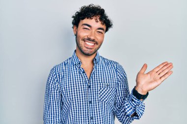 Gündelik kıyafetler giyen genç İspanyol adam neşeli bir şekilde gülümsüyor ve avuç içi kameraya bakıyor.. 