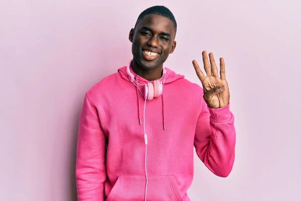 年轻的非洲裔美国人穿着运动服 用耳机展示和指点着四号手指 面带微笑 自信而快乐 — 图库照片
