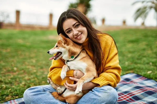 Güzel genç bir kadın parkta mutlu Shiba Inu köpeğine sarılıyor.