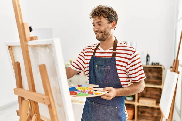 年轻的他惊慌失措的男人带着自信的笑容在艺术工作室里画画 — 图库照片