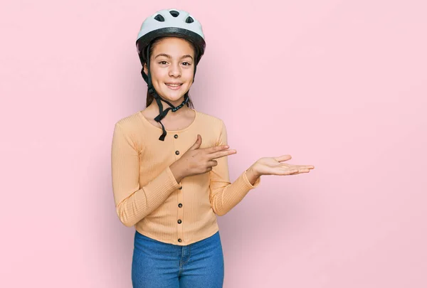 美しいブルネットの女の子を身に着けている自転車のヘルメット驚きと笑顔へカメラを提示しながら手と指差すと指 — ストック写真