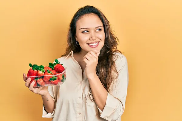 Chica Hispana Joven Sosteniendo Fresas Con Mano Barbilla Pensando Pregunta —  Fotos de Stock
