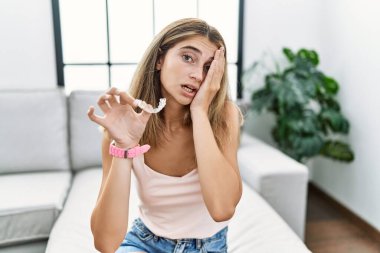 Görünmez hizada duran sarışın kadın ortodontik esneme yorgunluğu, yarı yüz, göz ve ağız kısmını eliyle kapatıyor. Yüzüm acıyor.. 