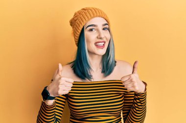 Yün şapka takan genç bir kız. Elleriyle olumlu jest yapıyor. Gülümsüyor ve mutlu. Neşeli ifade ve kazanan jest. 