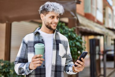 Genç İspanyol adam şehirde akıllı telefon kullanarak mutlu gülümsüyor..