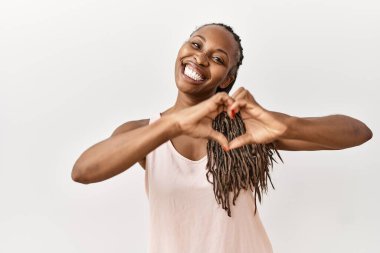 Saçları örgülü siyah bir kadın, izole edilmiş arka planda duruyor. Aşkla gülümsüyor, elleriyle kalp sembolü yapıyor. romantik kavram. 