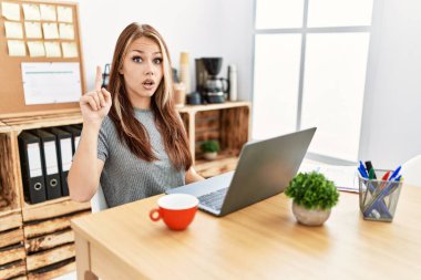 Ofiste çalışan genç esmer kadın dizüstü bilgisayarla başarılı bir fikri işaret ediyor. Heyecanlı ve mutlu. Bir numara.. 