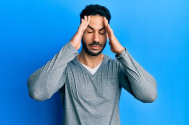 Latin asıllı genç bir adam, günlük beyaz tişört giyiyor, eli başının üstünde, stresten baş ağrısı çekiyor. migren ağrısı. 