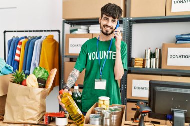 Gönüllü üniformalı genç İspanyol bir adam yardım merkezindeki akıllı telefondan konuşuyor..