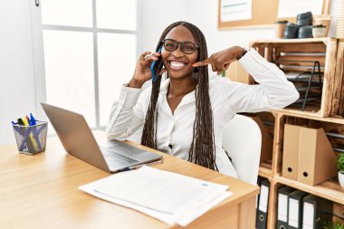 Ofiste çalışan, saçları örgülü, neşeli gülümseyen, parmaklarıyla ve ağzıyla gülümseyen zenci bir kadın. diş sağlığı kavramı. 