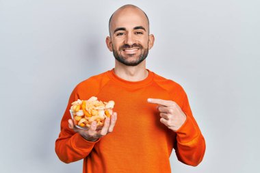 Patates cipsi tutan genç kel adam gülümsüyor. 