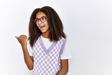Young african american girl standing over isolated background smiling with happy face looking and pointing to the side with thumb up. 