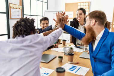 Bir grup işçi ofiste el ele kutlama yaparken gülümsüyor..