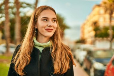 Genç sarışın kız gülümsüyor, mutlu bir şekilde şehirde duruyor..