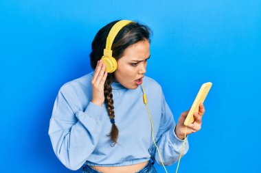 Akıllı telefon ve kulaklık kullanan genç İspanyol kız, şaşkın ve alaycı görünüyor, ağzı açık kalınca şaşırıyor. 