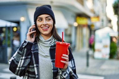 Genç İspanyol kadın akıllı telefondan konuşuyor. Şehirde soda içiyor..