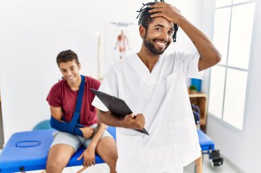 Kırık kollu, kendine güvenen, el hareketleriyle saçlarına dokunan, çekici ve modaya uygun pozlar veren bir adamla birlikte ağrı kesici kliniğinde çalışan İspanyol genç bir adam. 