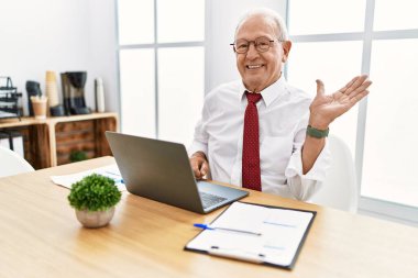Ofiste çalışan son sınıf öğrencisi bilgisayarı kullanıyor. Gülümsüyor, gülümsüyor ve avuç içi kameraya bakıyor.. 